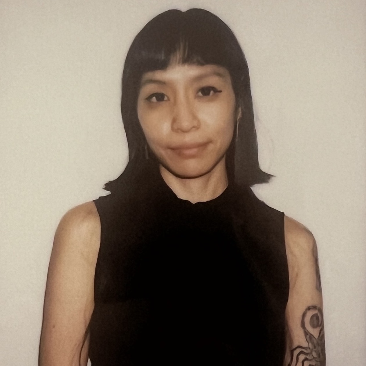 A instax photo of Cella wearing a black sleeveless button down shirt